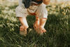 Baby mit nackten Füßen wird von Elternteil über eine Wiese gehalten