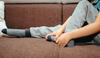 Kind liegt auf der Couch und hält mit beiden Händen den linken Fuß fest