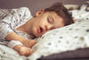 Kind schläft mit halb offenem Mund auf der Seite im Bett