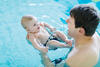 Vater hält Baby auf dem Rücken im Wasser und spricht mit ihm