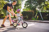 Vater in Sommerkleidung schubst Kleinkind auf dem Fahrrad sanft anan