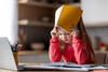 Mädchen im Grundschulalter macht Hausaufgaben und zieht sich dabei das Heft wie einen Hut über den Kopf. Sie wirkt unkonzentriert.