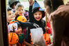 Kindergruppe steht in Halloween-Kostümen vor einer Haustür und bekommt Süßigkeiten von einer Mutter