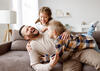 Zwei Kinder toben mit ihrem Vater auf dem Sofa