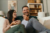 Frau und Mann sitzen lachend auf der Couch und essen Popcorn